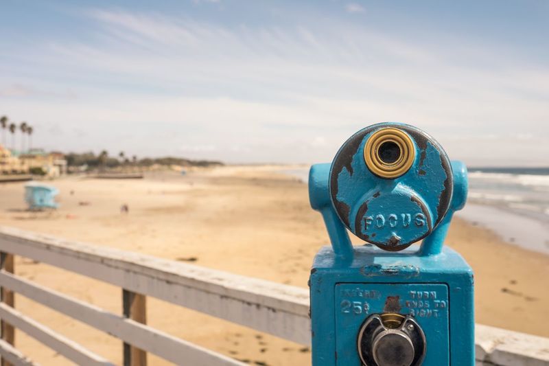 Coin-operated binocular on pier at sandy beach against sky