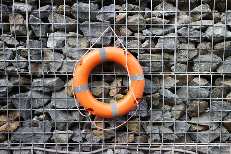 Orange life belt hanging on metal grate by stones