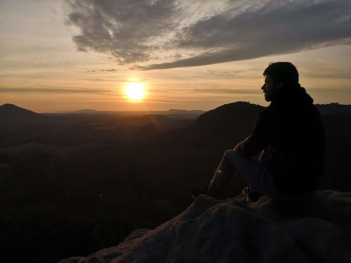 Side view of man sitting on rock at sunset