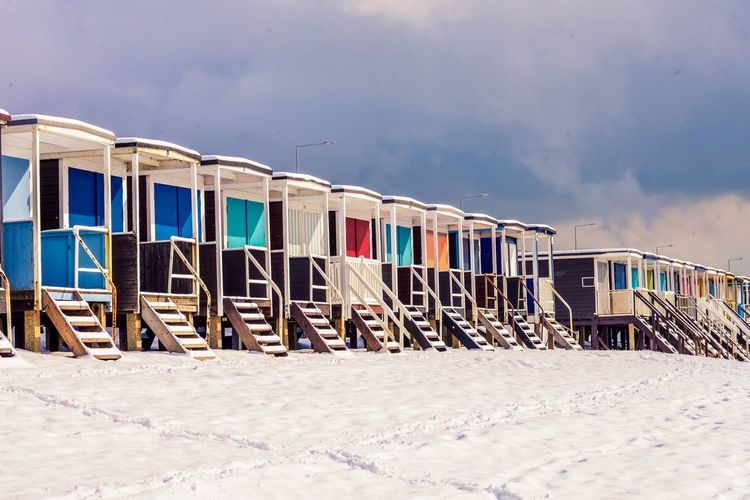 Snow on beach  and coloured beach huts against sky