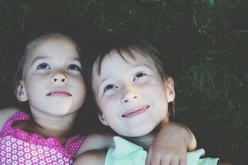 Close up portrait of two cute little girls laying on grass, deep in thoughts and dreams