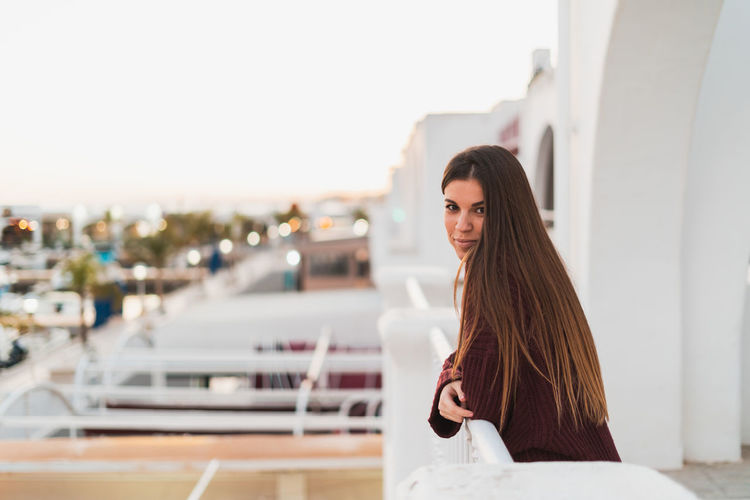 Portrait of young woman standing in balcony against clear sky