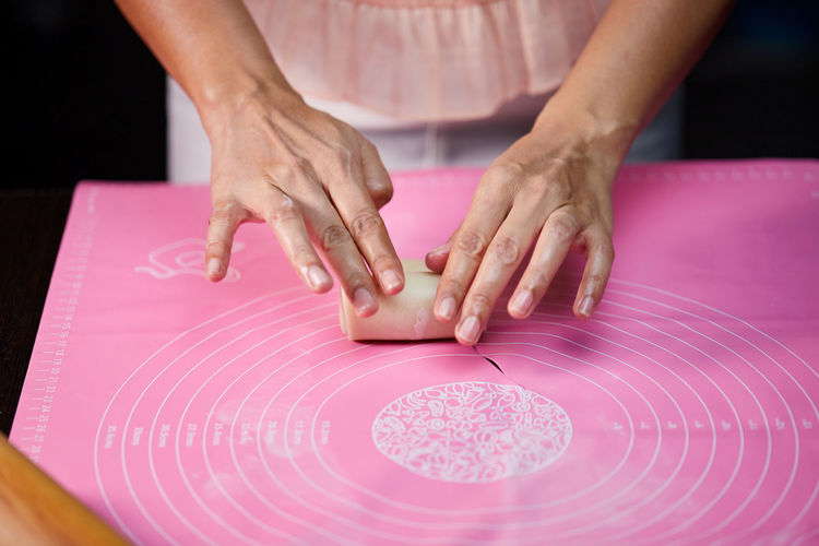 Woman's hands molding the rolle shape dough on pink silicone mesh