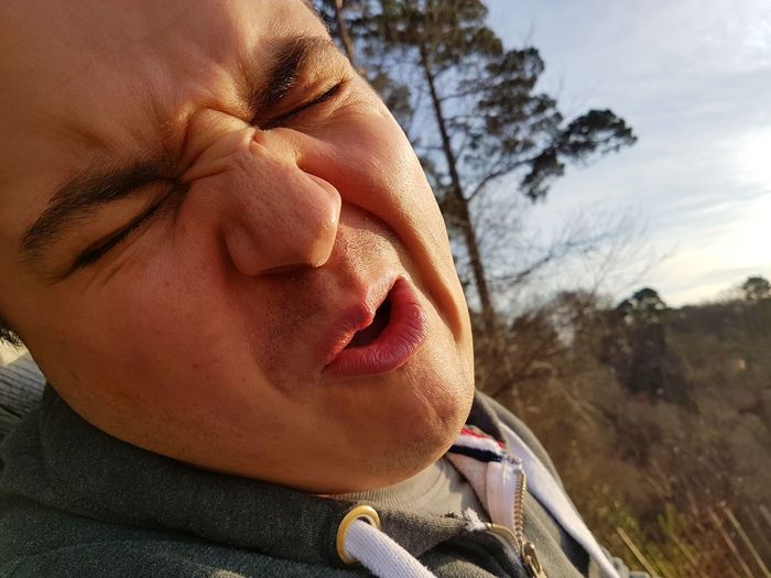 Close-up of young man making face against sky