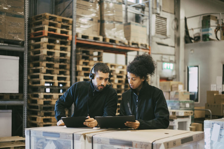 Male and female colleagues discussing while using digital tablet at logistics warehouse