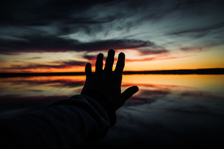 Cropped hand gesturing against sky during sunset