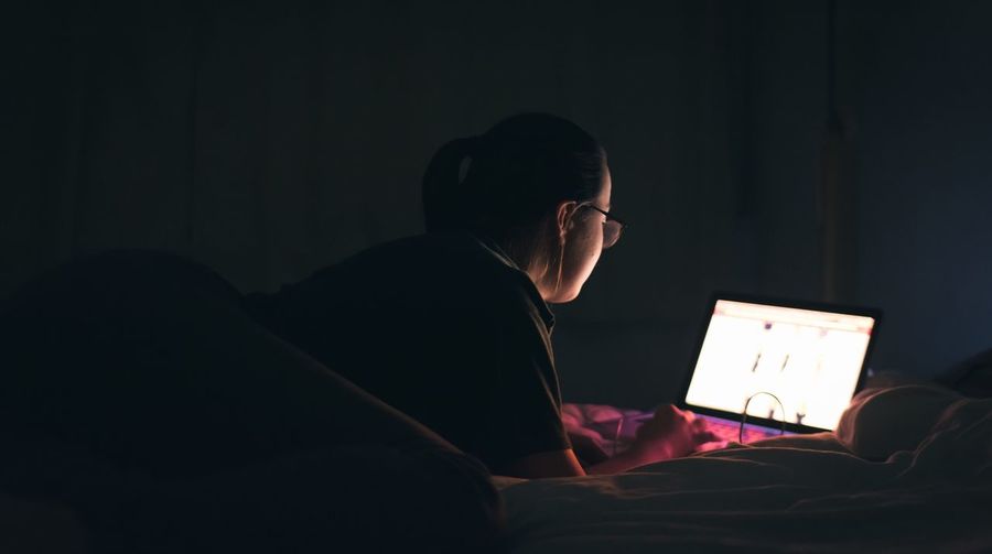 Rear view of woman using laptop on bed