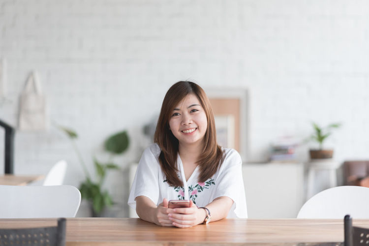 Portrait of smiling young woman sitting by table at home