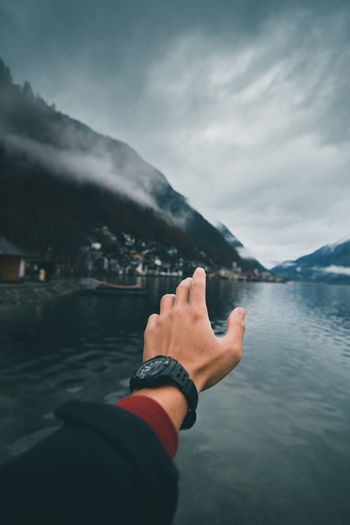 Cropped hand of man at lake against mountain range