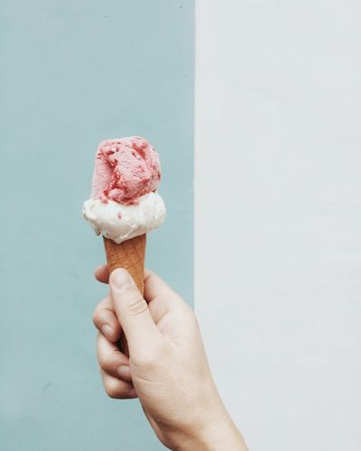 Cropped hand holding ice cream against colored background