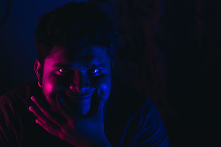 Close-up of young man smiling in multi colored lights against black background