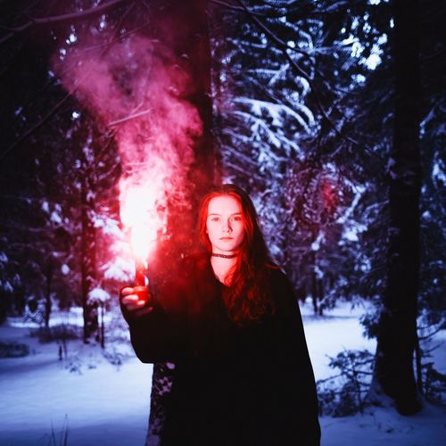 Portrait of woman holding distress flare while standing against trees