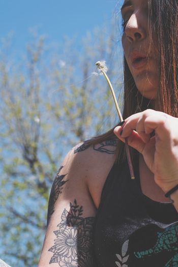Low angle view of woman blowing dandelion seeds against tree