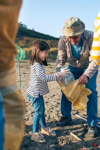 Granddaughter assisting grandfather while cleaning beach