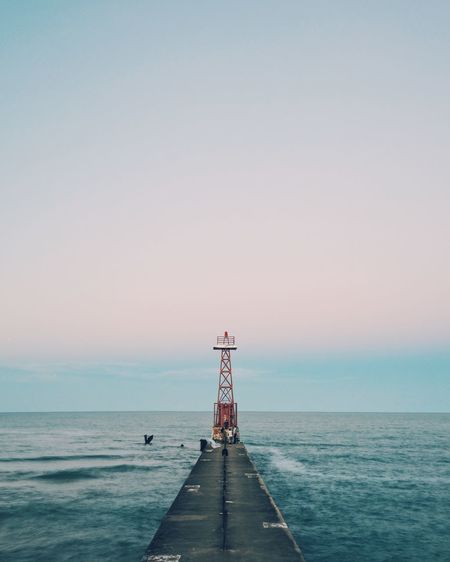 Pier leading towards lookout tower against sea and sky at dusk