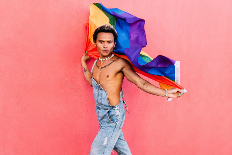 Portrait of man carrying rainbow flag against colored background