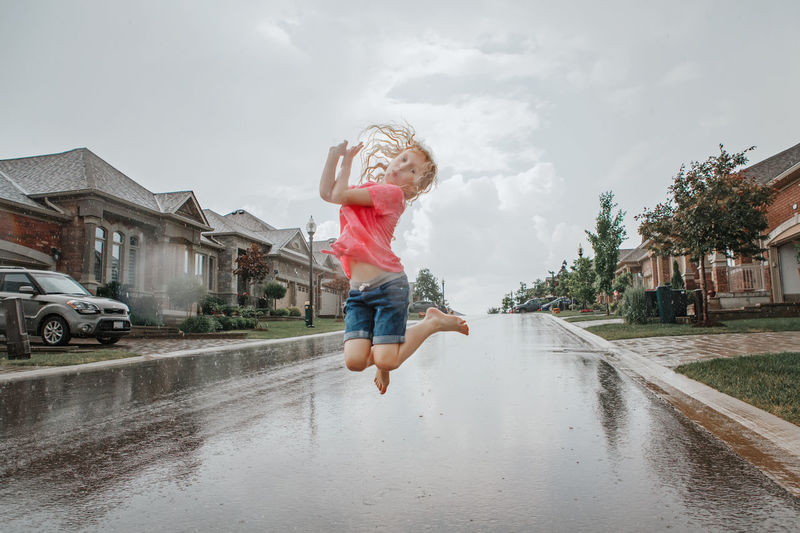 Girl running splashing under rain on street road. child having fun during rain shower storm