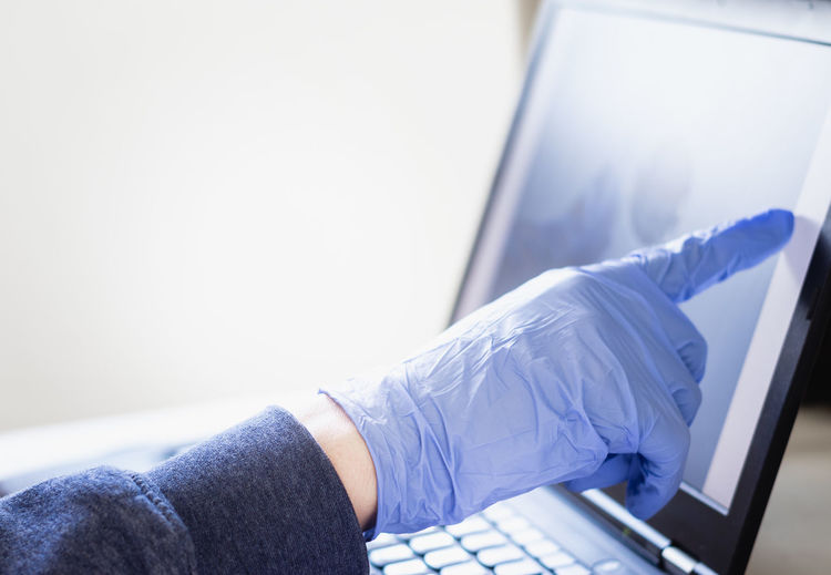 Blue gloves touches a laptop screen, working from home in the corona