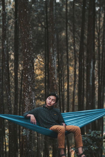 Young man sitting on hammock in forest