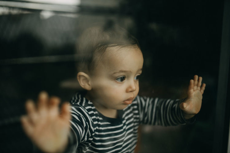 Portrait of cute boy looking through window glass