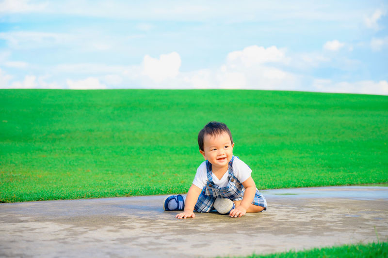 Portrait of cute boy on grass against sky