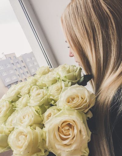 Side view of woman holding white rose bouquet while looking through window at home