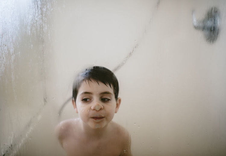 Shirtless boy pressing nose on condensed window in bathroom