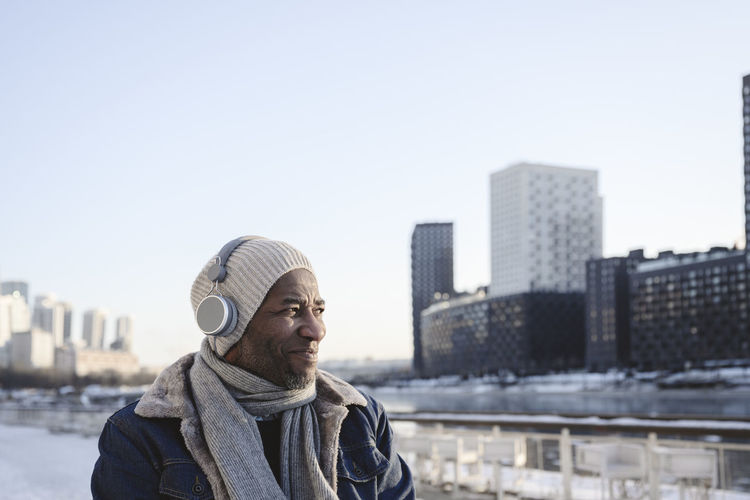 Smiling man listening music through wireless headphones with city in background