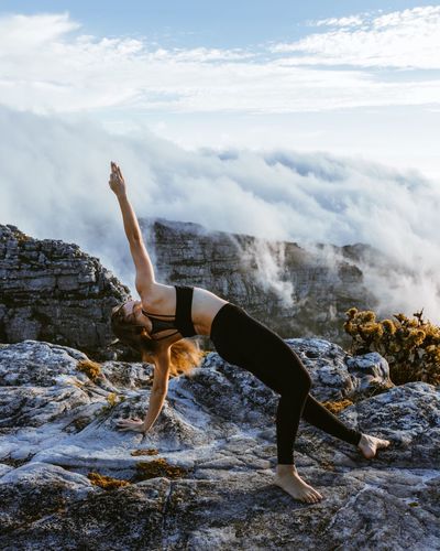 Woman practicing yoga on rock formation against sky during sunset