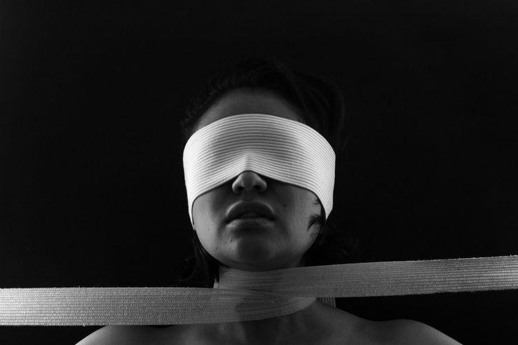 Close-up of young woman eyes covered with bandage against black background