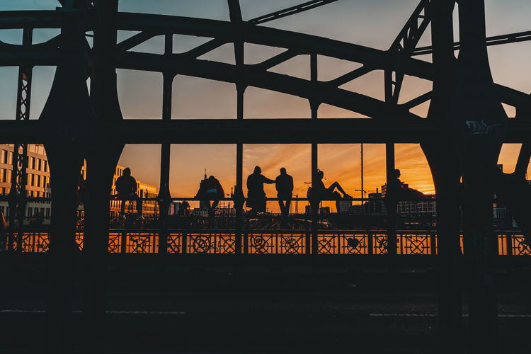 Silhouette people on bridge in city against sky during sunset