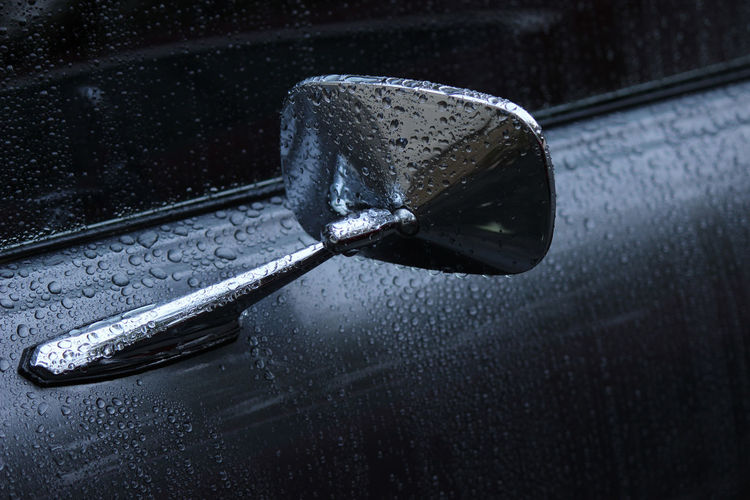Close-up of wet side-view mirror on car door during rain