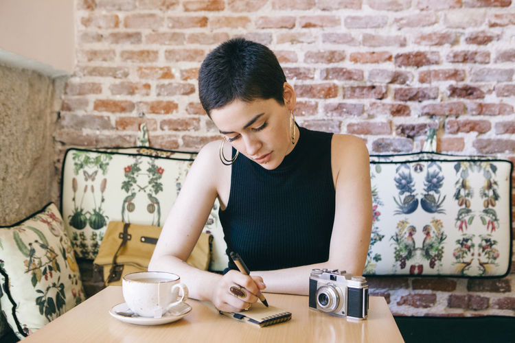 Young woman with short hair writing on note pad in cafe