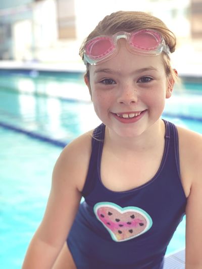 Portrait of smiling girl sitting against swimming pool