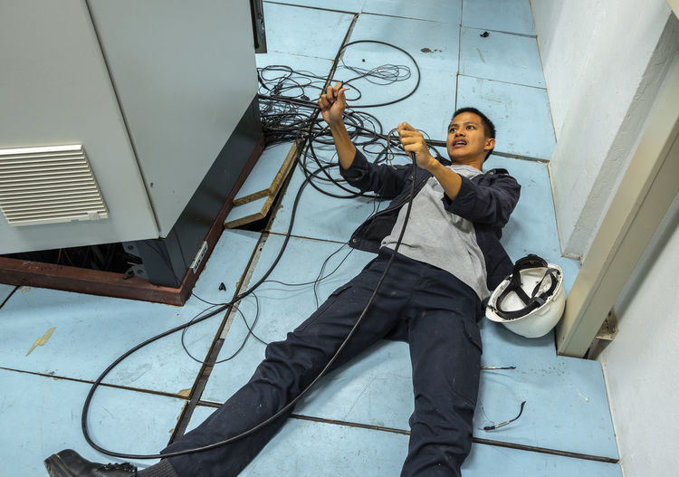 Shocked man holding cables while lying on floor by fuse box