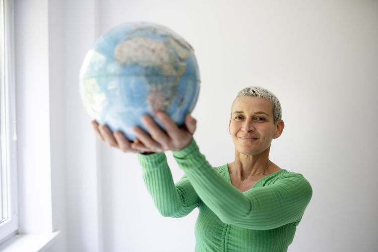 Portrait of young woman holding globe against white background