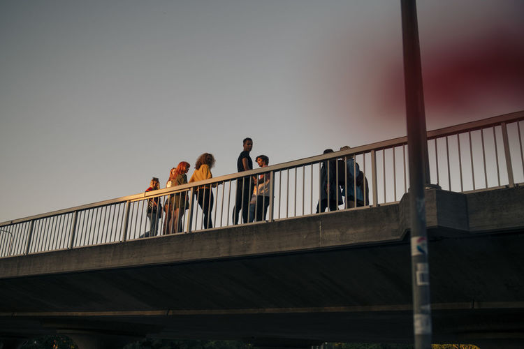 Low angle view of people walking on footbridge against clear sky