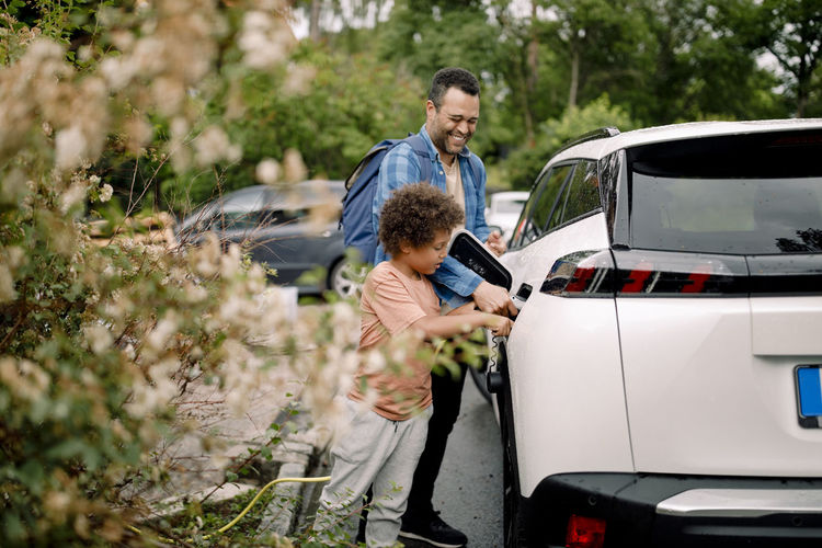 Smiling man with son charging electric car