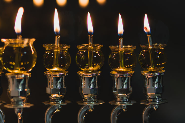 Hanukkah candles are lit in a silver-decorated menorah, against a black background of the night 