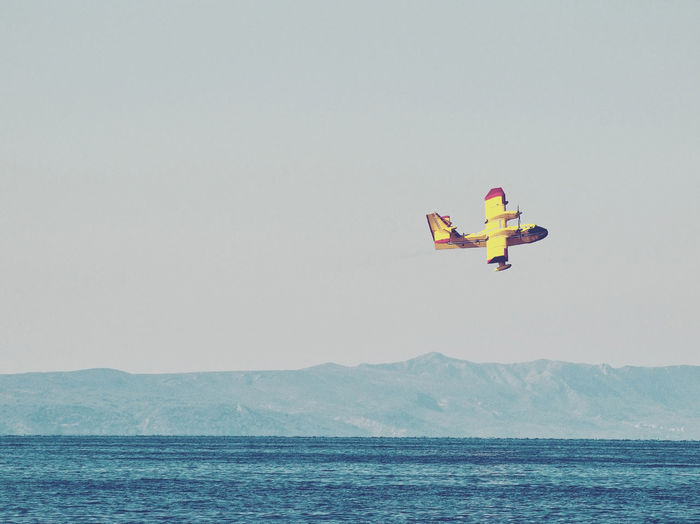 Firefighting aircraft flying over sea against clear sky