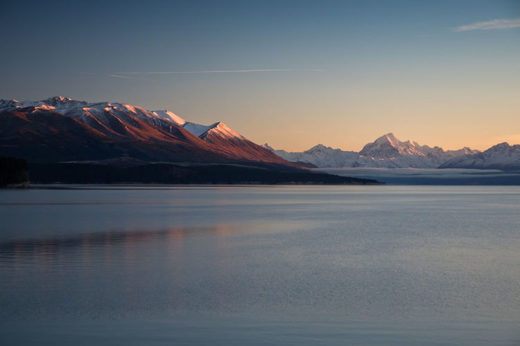 Scenic view of lake and snowcapped mountains against sky during sunset