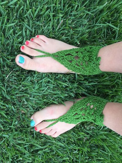 Low section of woman wearing woolen sandals while standing on grassy field
