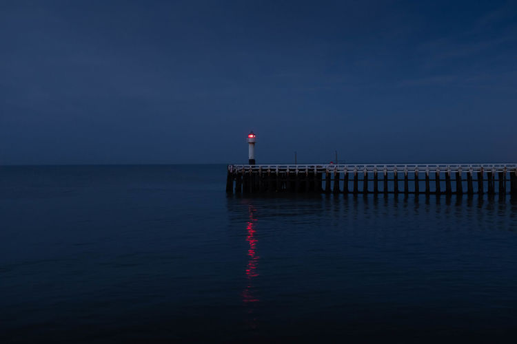 Lighthouse on pier by sea against sky