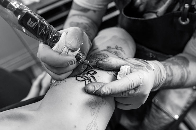 Cropped image of artist making tattoo on hand of customer
