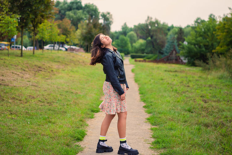 Very beautiful young girl smiling, closing her eyes and raising her head up in a green park