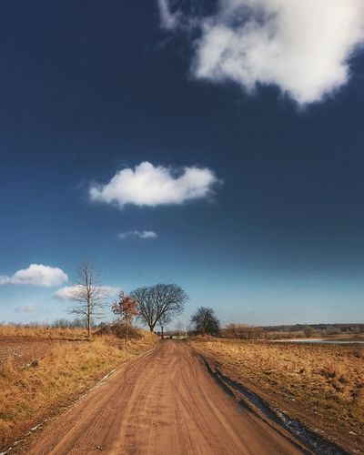 Road amidst field against blue sky