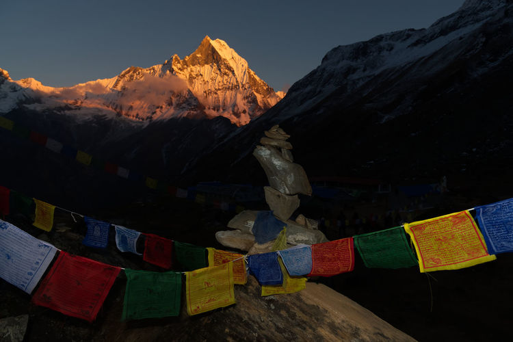 Multi colored tibetan flags on snowcapped mountains against sky at sunset