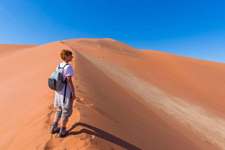 Full length of woman standing on desert against clear blue sky