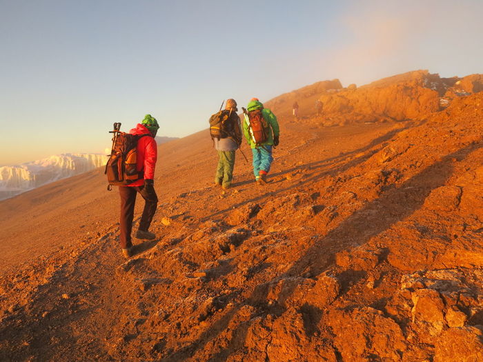 Rear view of hikers with backpack climbing mountain against sky during sunset