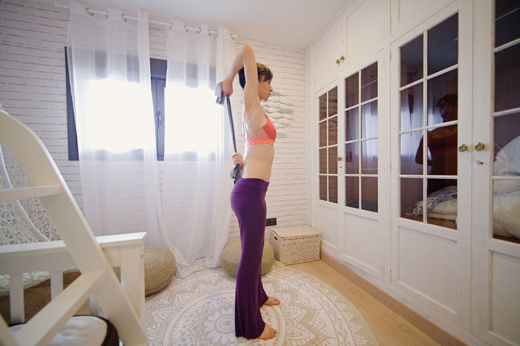 Side view of woman exercising while standing at home